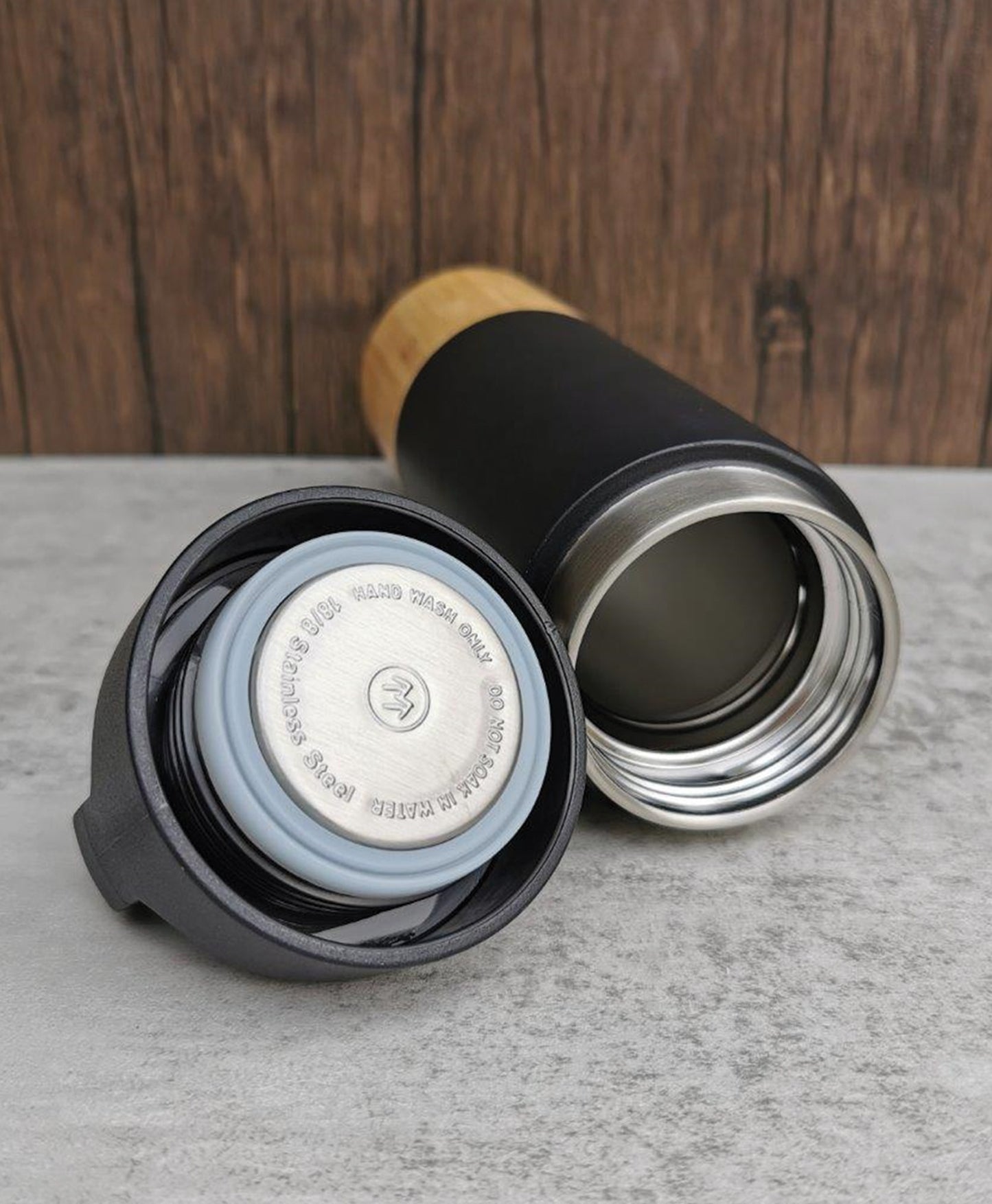 Bamboo Bottom Insulated Stainless Steel Bottle showing open lid and interior with wooden background and concrete surface.