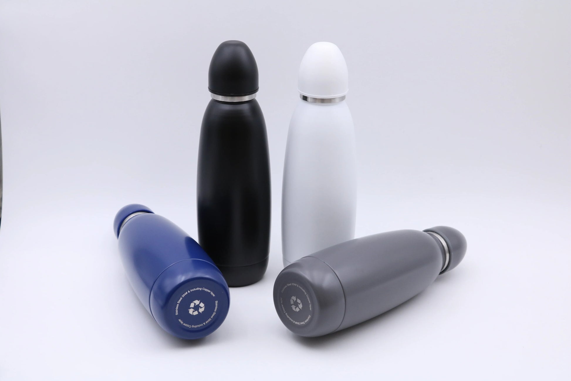 Four sleek Bullet Bottle insulated stainless steel water bottles in black, white, blue, and gray colors on a flat surface.