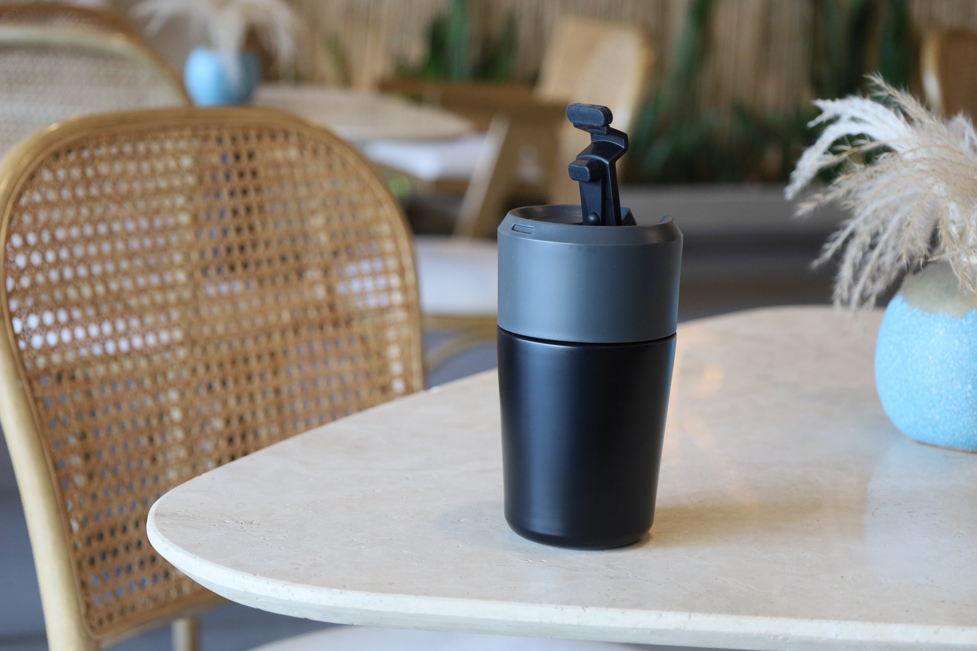 Black Vacuum Mug with flip-top lid placed on a marble table in a cozy indoor setting